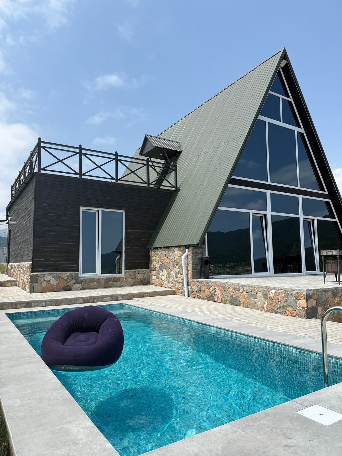 The house with its triangular glass facade, terrace and pool on a sunny day