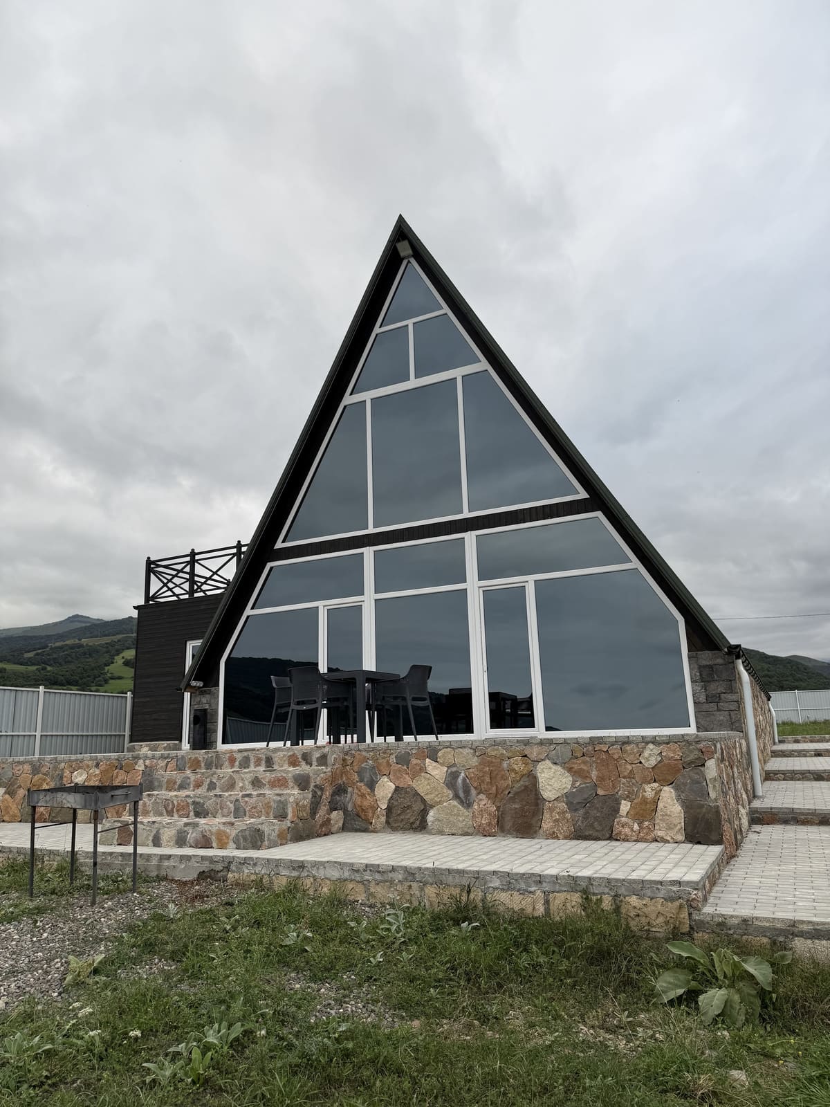The triangular glass facade of the house on its stone base on an overcast day