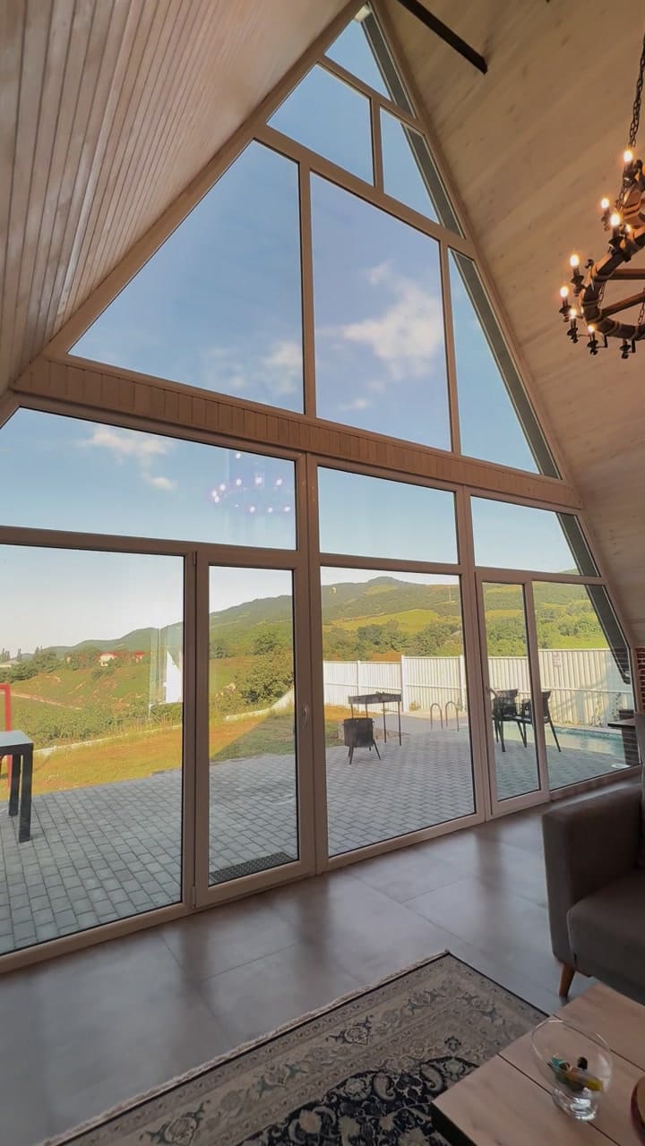 The triangular glass facade of the living room from inside, with the terrace and mountain slopes beyond